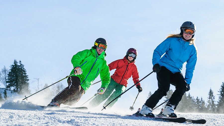 Drei Skifahrerinnen und Skifahrer auf der Piste bei schönem Wetter