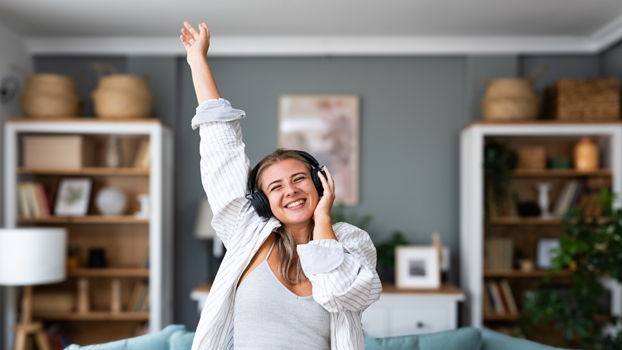 Junge Frau mit Kopfhörer tanzt in einer Wohnung