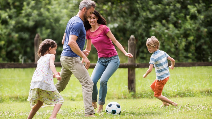 Mann, Frau und zwei Kinder spielen Fußball auf einer Wiese