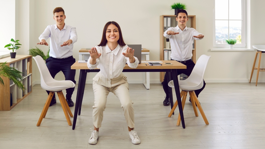 Drei Personen in Business-Kleidung bei sportlichen Übungen im Büro
