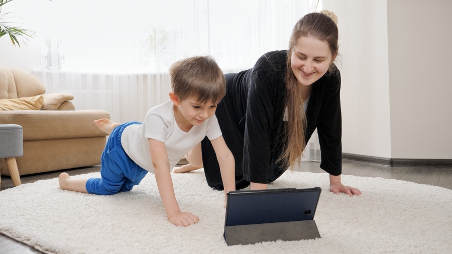 Mutter und Kind turnen gemeinsam vor einem aufgestellten Tablet