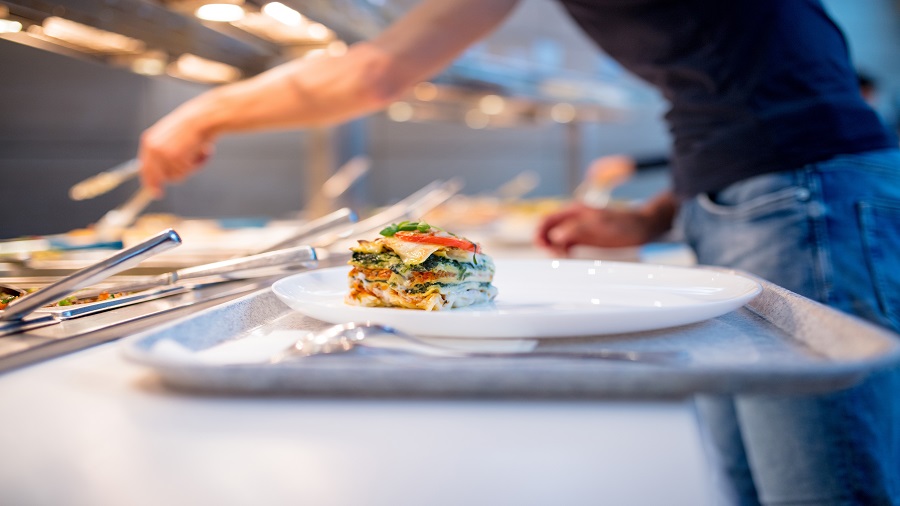 Essen auf einem Teller und Tablett mit einem Mensch im Hintergrund, der sich am Buffet bedient.
