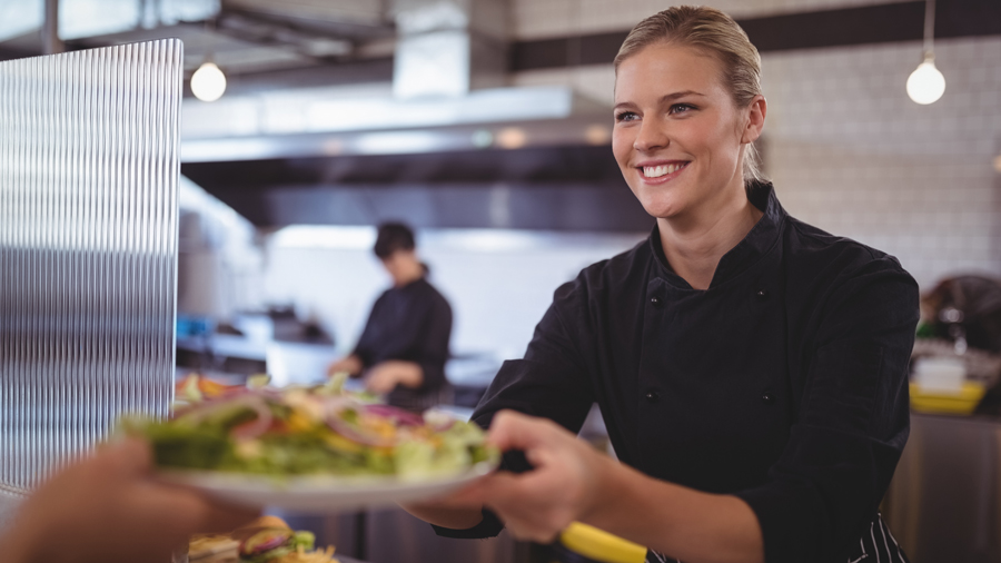 Frau reicht einen Teller in einer Kantine über die Theke