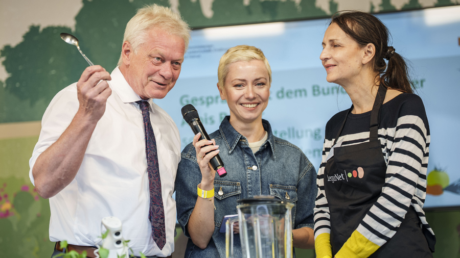 Bundeslandwirtschaftsminister Alois Reiner, eine Moderatorin und eine Mitarbeiterin des Projekts LeguNet auf einer Bühne