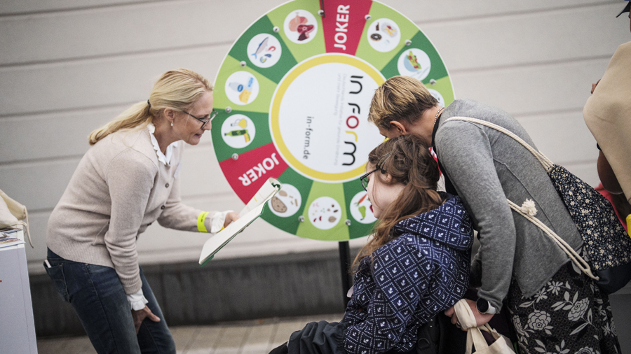Drei Frauen vor einem Glücksrad, eine davon sitzt im Rollstuhl