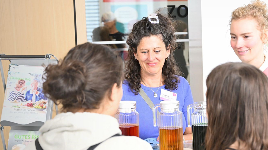Zwei Frauen hinter einem Messestand im Gespräch mit zwei jungen Frauen