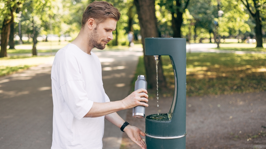 Mann füllt Wasserflasche an öffentlichem Wasserspender im Park