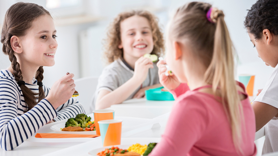Drei Mädchen und ein Junge in einer Schulkantine beim Mittagessen