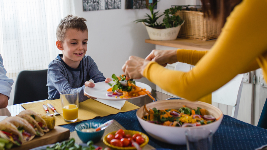 Frau (nur Arm zu sehen) füllt einem Jungen Salat auf einen Teller