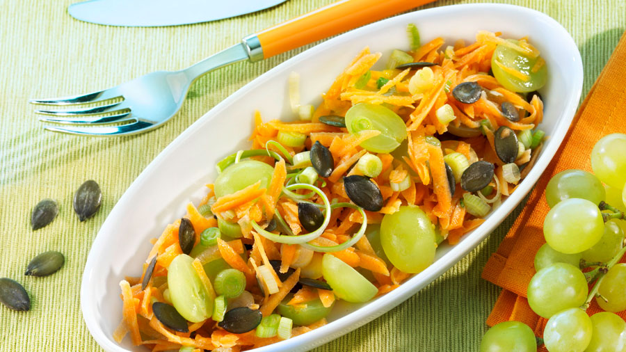 Eine große Schale mit Karotten-Lauchsalat mit hellen Weintrauben. Dekoriert mit Trauben und  Kürbiskernen.