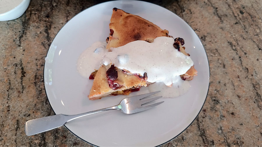 Ein Stück Clafoutis mit Joghurt serviert auf einen weißen Kuckenteller mit Gabel.