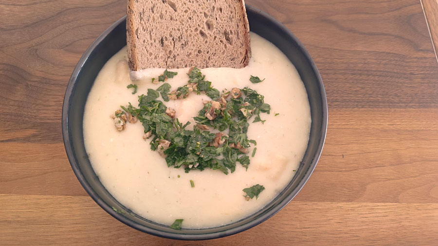 Cremige Spargelsuppe mit Nuss-Topping und einer Scheibe Vollkornbrot serviert