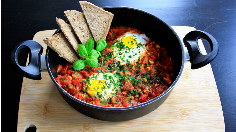 1 Topf Shakshuka mit 4 Scheiben Vollkorntoast serviert auf einem Holzbrett.