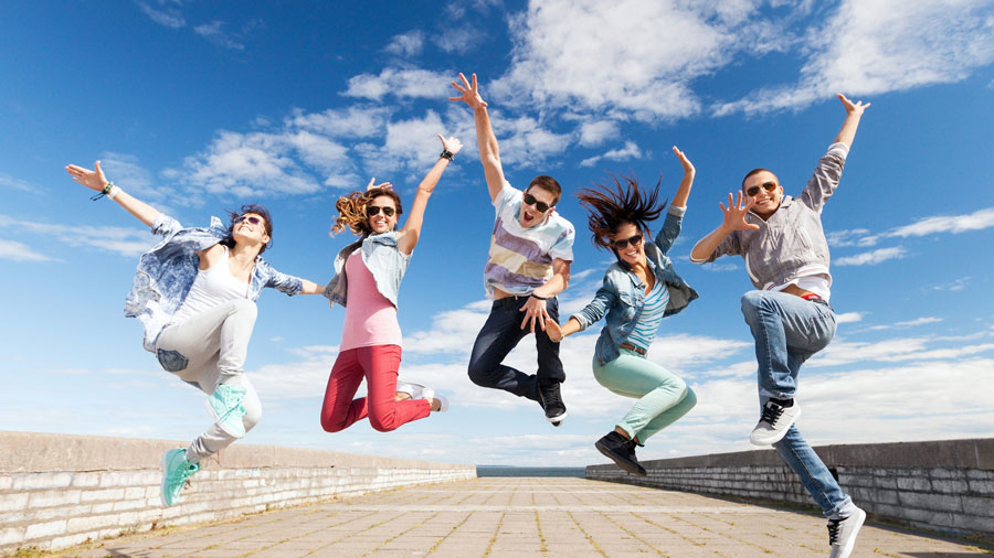 5 junge Erwachsene springen mit Freude in die Luft. Blauer Himmel mit wenig Wolken.