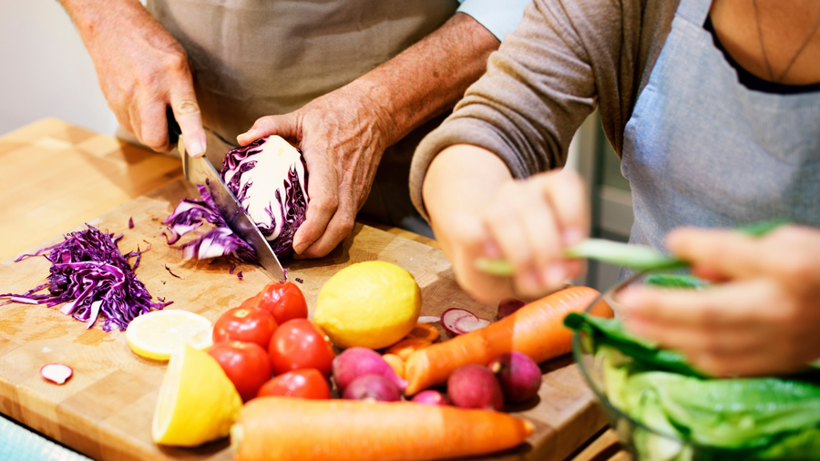 Hände älterer Personen schneiden Gemüse auf einem Holzbrett