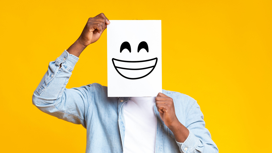 Männerhände halten sich ein Bild mit einem lachenden Smily vor das Gesicht