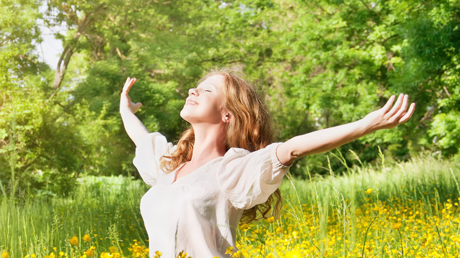 Frau reckt die Arme hoch auf einer grünen Wiese