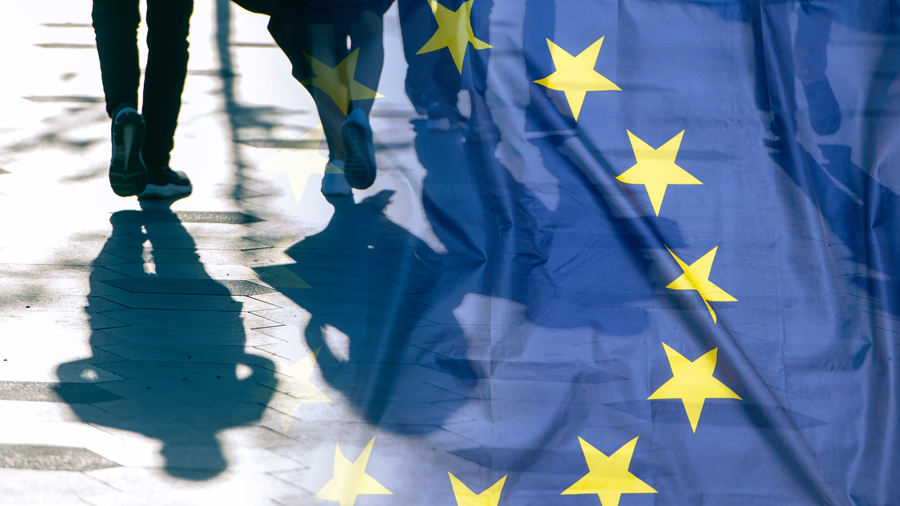 Blaue EU-Fahne mit Sternen, daben Schatten von gehenden Menschen