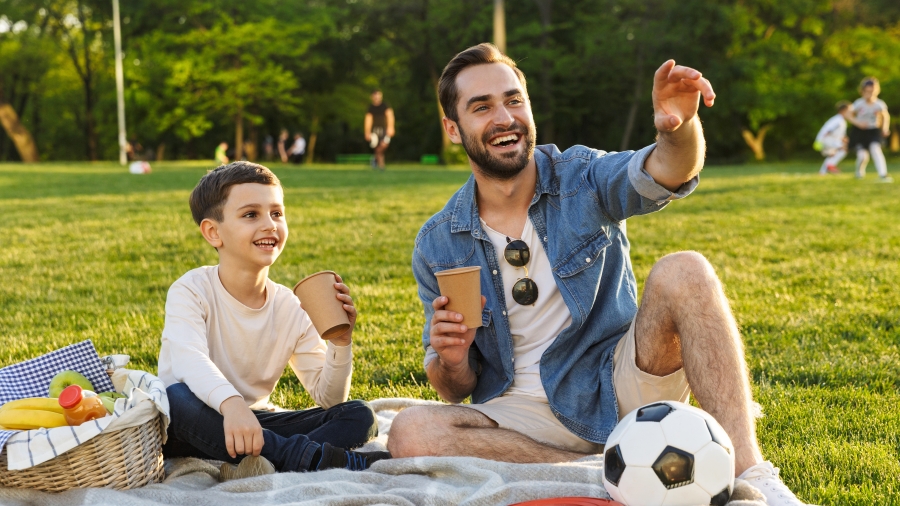 Vater und Sohn beim Piknick, vor ihnen ein Fußball und eine Frisbeee-Scheibe