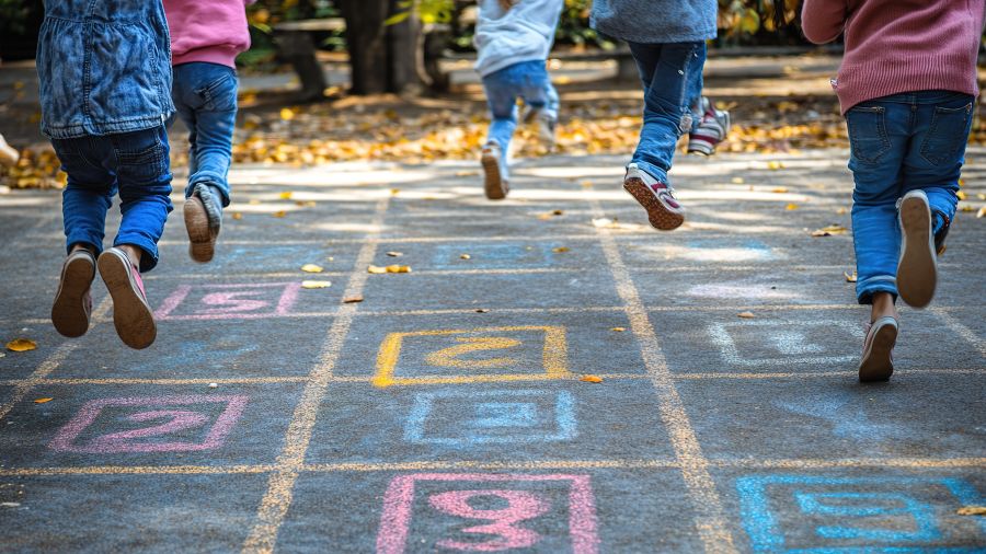 Hüpfspiel - Kinderbeie hüpfen auf bunten Quadraten auf dem Asphalt