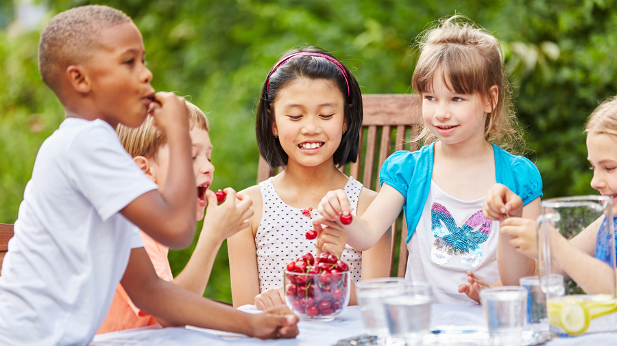 Fünf Kinder sitzen am Tisch und essen Kirschen