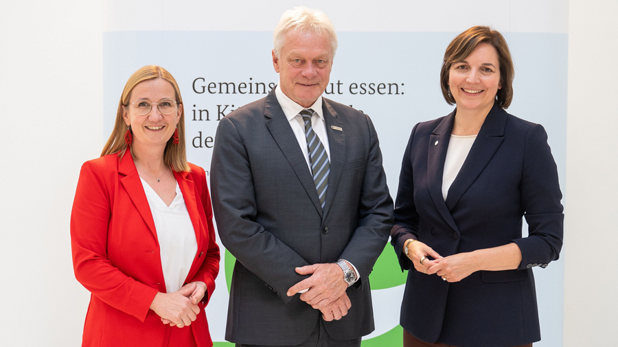 Drei Personen vor dem Plakat des Kongresses mit dem Motto "Alle an einen Tisch"