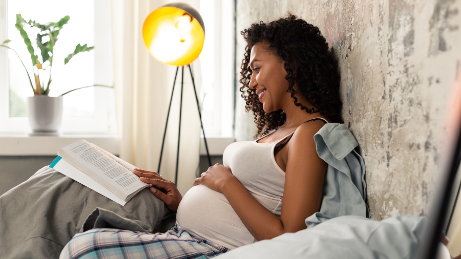 Schwangere Frau sitz auf einem Bett und liest eine Zeitschrift