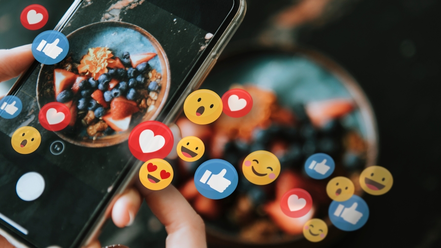 Handy halten ein Smartphone, darum fliegen einige Emoji wie Herzen und "Gefällt mir"-Daumen