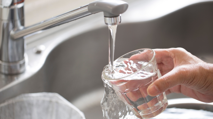 Hand füllt ein Wasserglas unter einem Wasserhahn in einer Spüle
