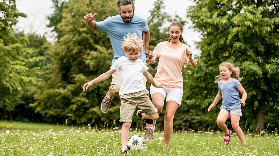 Mann, Frau und zwei Kinder spielen Fußball auf einer Wiese
