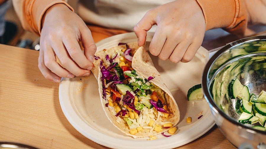 Kinderhände falten einen Wrap mit vegetarischen Zutaten zusammen