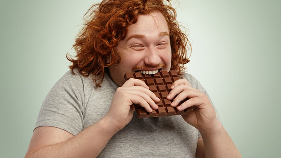 Mann mit rotem, lockigem Haar beisst genussvoll in eine Tafel Schokolade