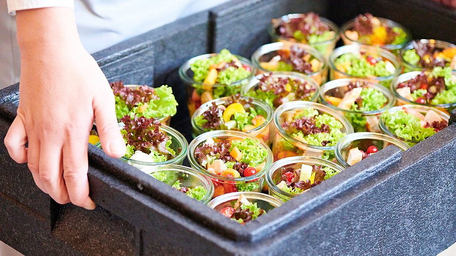 Hände halten einen Behälter mit Salatportionen in Gläsern