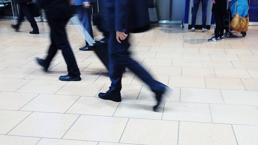 Symbolbild reisestress: Verwischte Aufnahme von Beinen in Businesskleidung, die sich hektisch bewegen