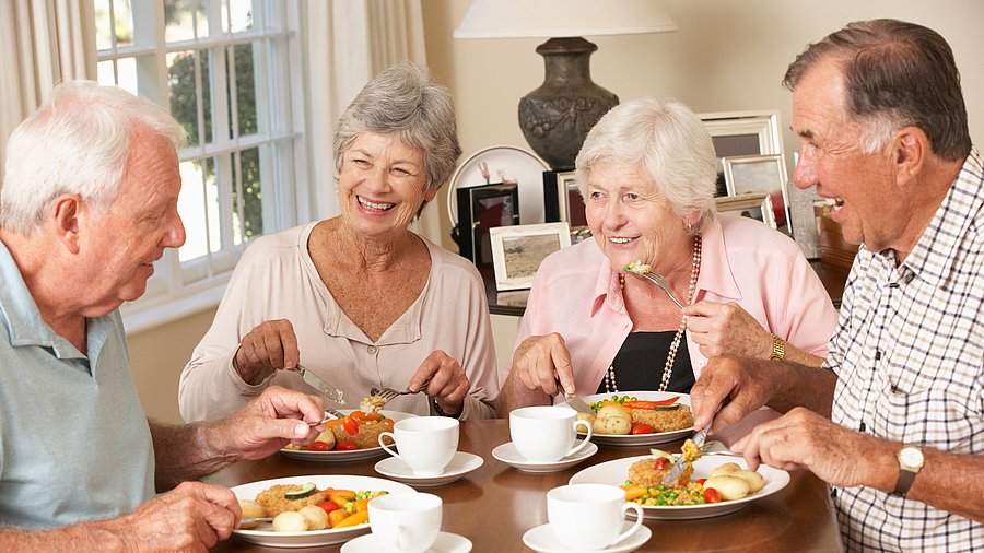 Zwei ältere Frauen und zwei altere Männer sitzen lachend am Tisch und essen zu Mittag