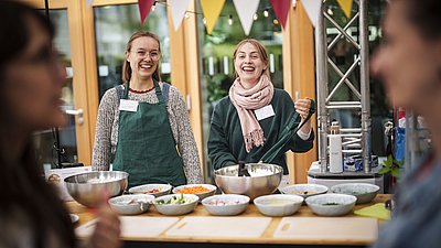 Zwei Frauen an einem Tisch, auf denen mehrere Schalen mit Essenszutaten stehen