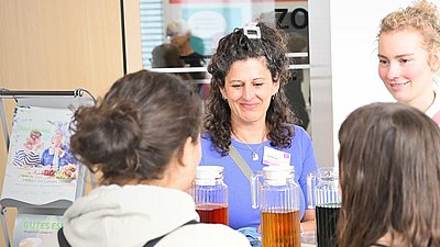 Zwei Frauen hinter einem Messestand im Gespräch mit zwei jungen Frauen