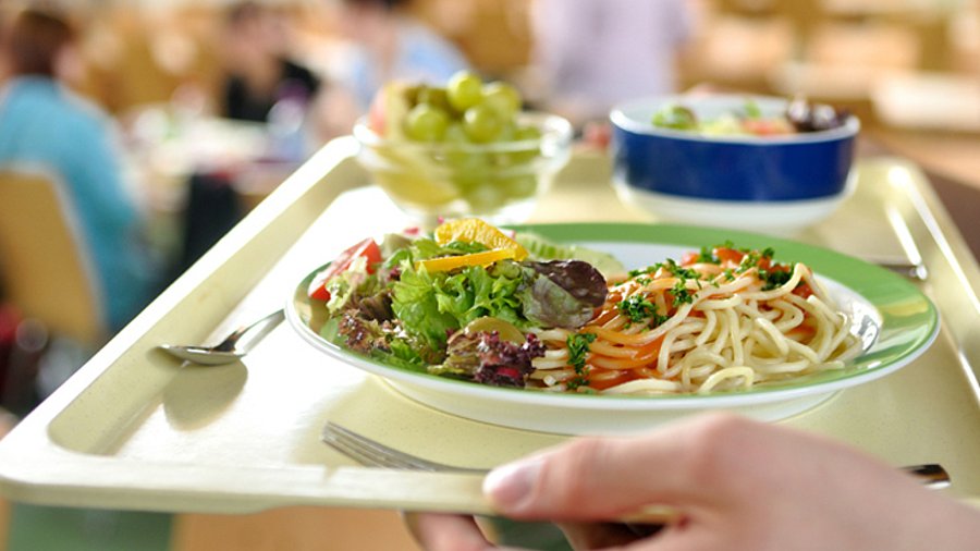 Hände halten ein Essenstablett mit einem Pastagericht und Salat