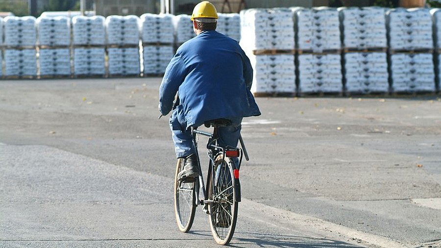 Mann mit Arbeitskleidung und Bauhelm auf einem Fahrrad