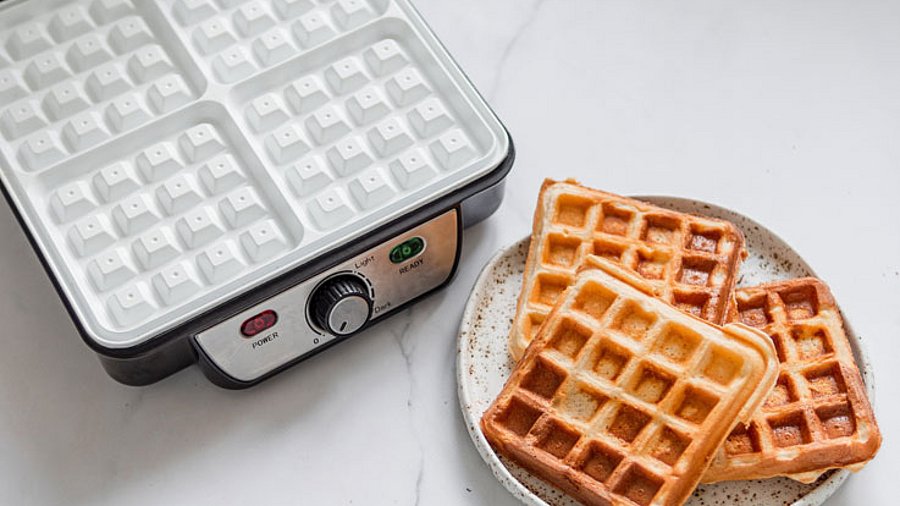 3 Stück frische Wafflen und ein Waffeleisen.