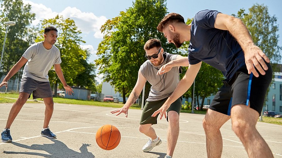 Drei Männer die zusammen Basketball spielen.