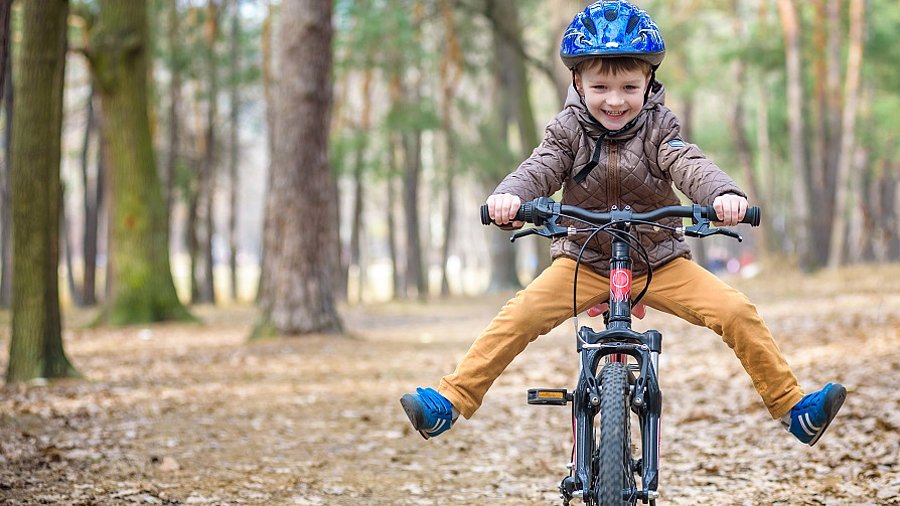 Lachender Junge auf einem Fahrrad im Wald.