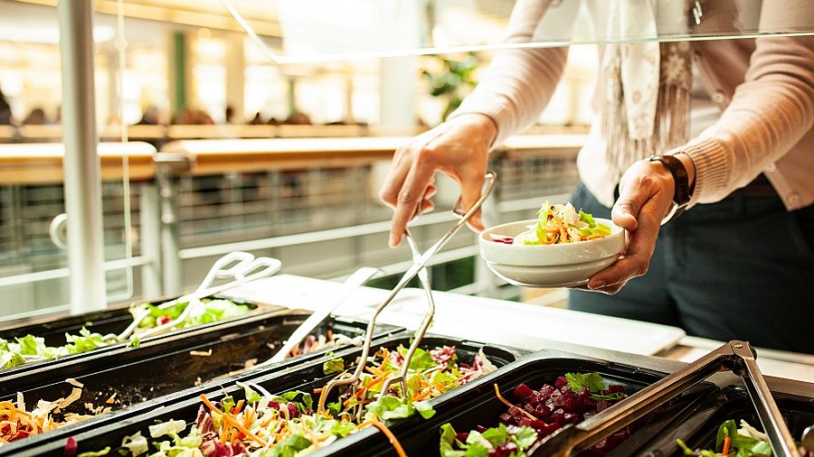 Frau bedient sich an einem Salatbuffet in einer Kantine