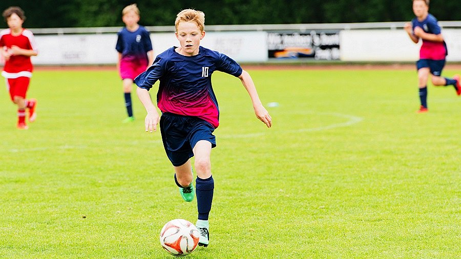 Junge in Trikot spielt Fußball auf einem Fußballfeld.