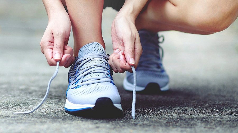 Ausschnitt von Laufschuhen, die von Frauenhänden auf der Straße gebunden werden.