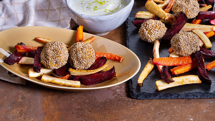 1 Teller mit Falafel und daneben ein Blech mit dem Gericht.