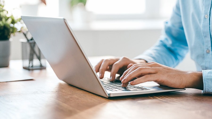 Im Fokus ein Laptop, auf dem ein Mann tippt.