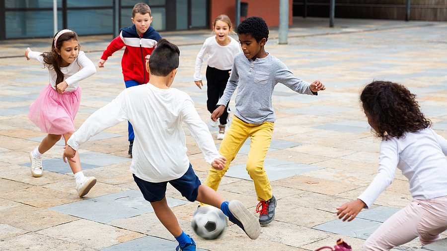 Drei Mädchen und drei Jungen spielen zusammen Fussball