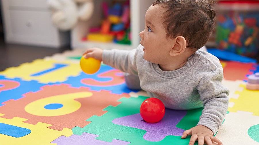 Baby liegt in Bauchlage auf einer bunten Matte