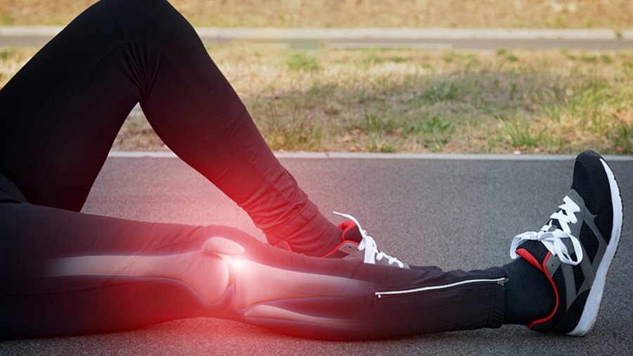 Beine in Sporthose auf einer Aschenbahn, Kniebereich rötlich markiert in der Art eines Röntgenbilds